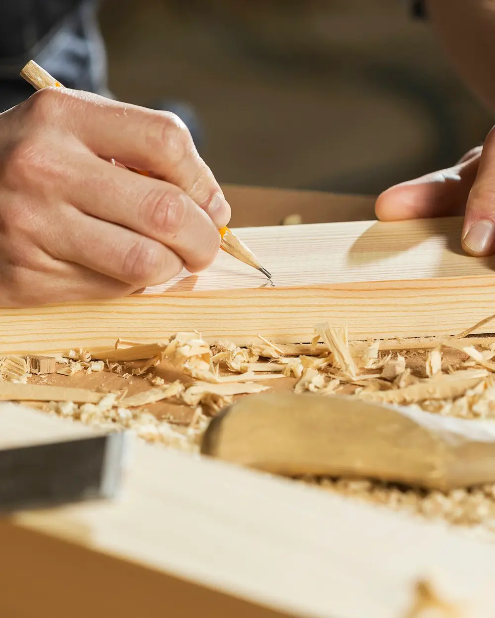 Carpenter marking a board with a pencil amid fresh wood shavings