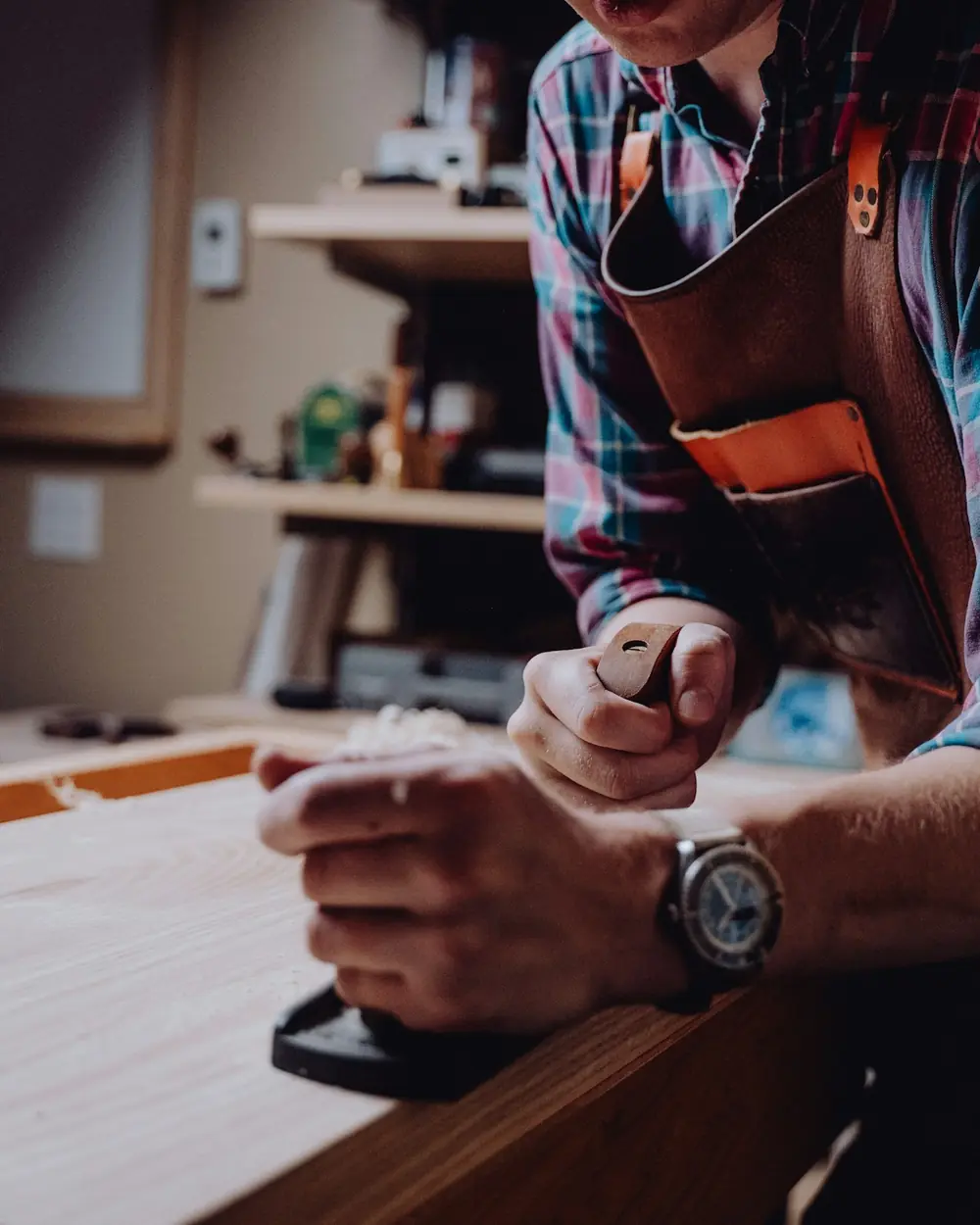 Woodworker in a leather apron planing a board at the workbench