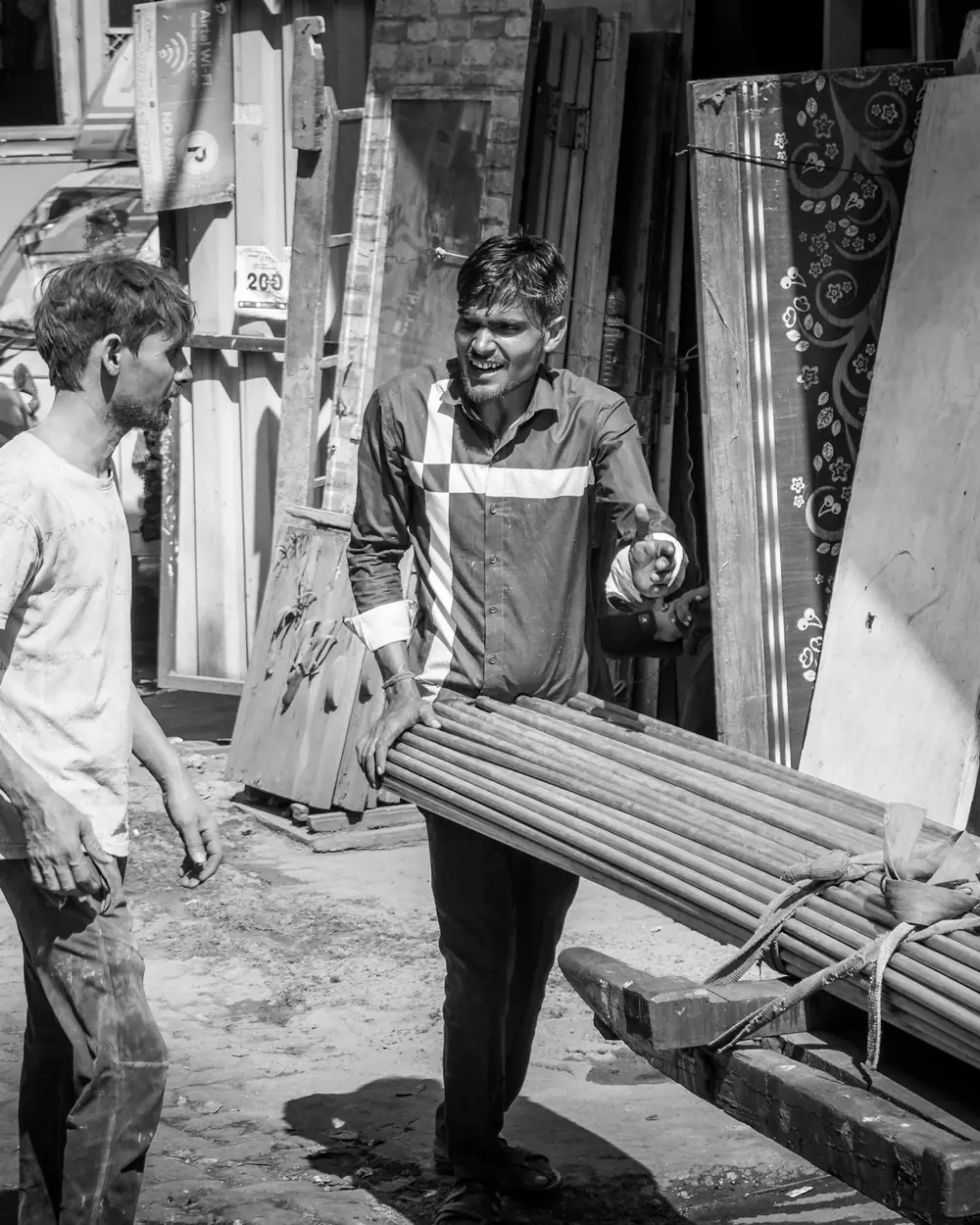 Two workers carrying seasoned timber planks through a timber market