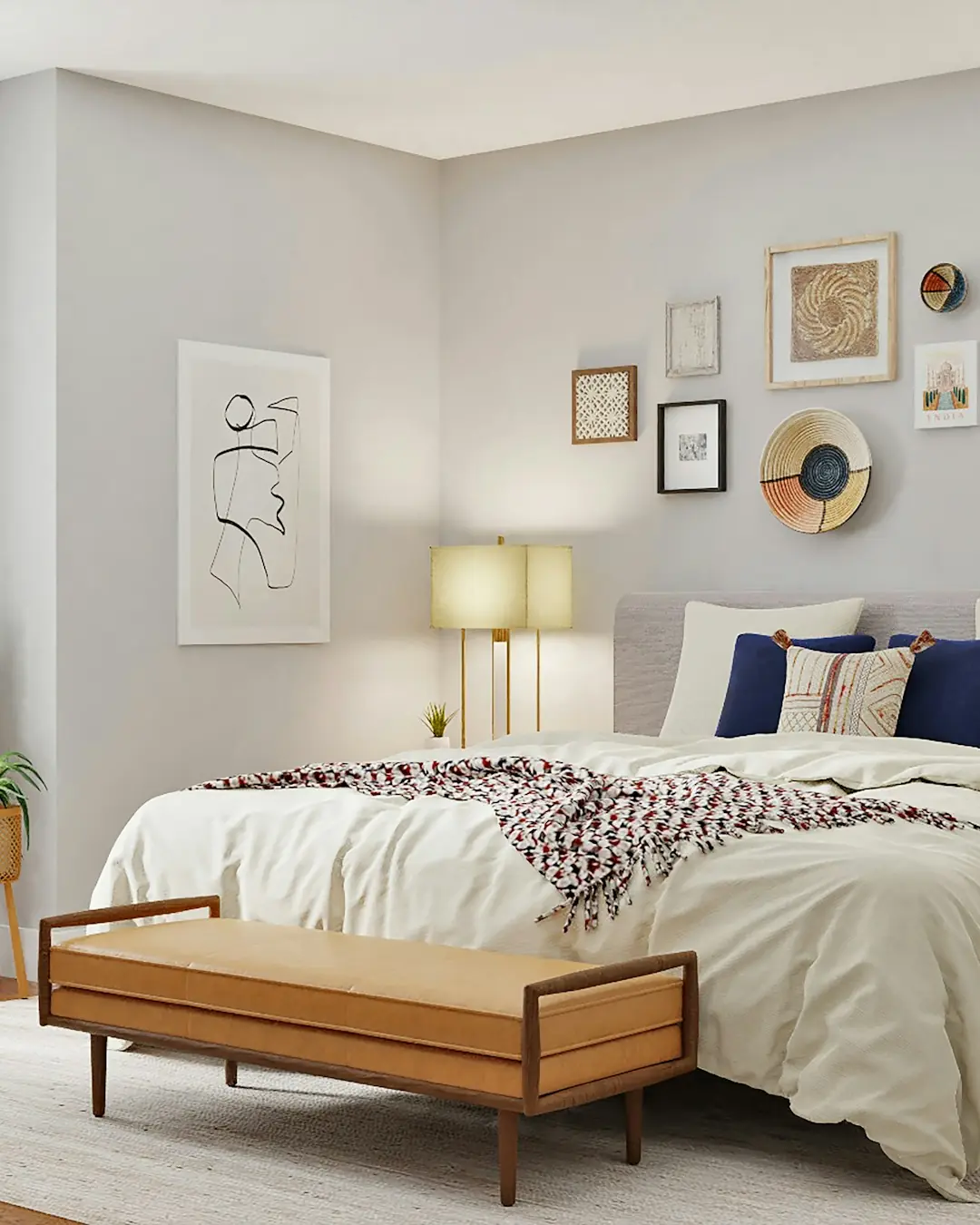 Calm bedroom with a gallery wall, layered bedding and a wooden bench