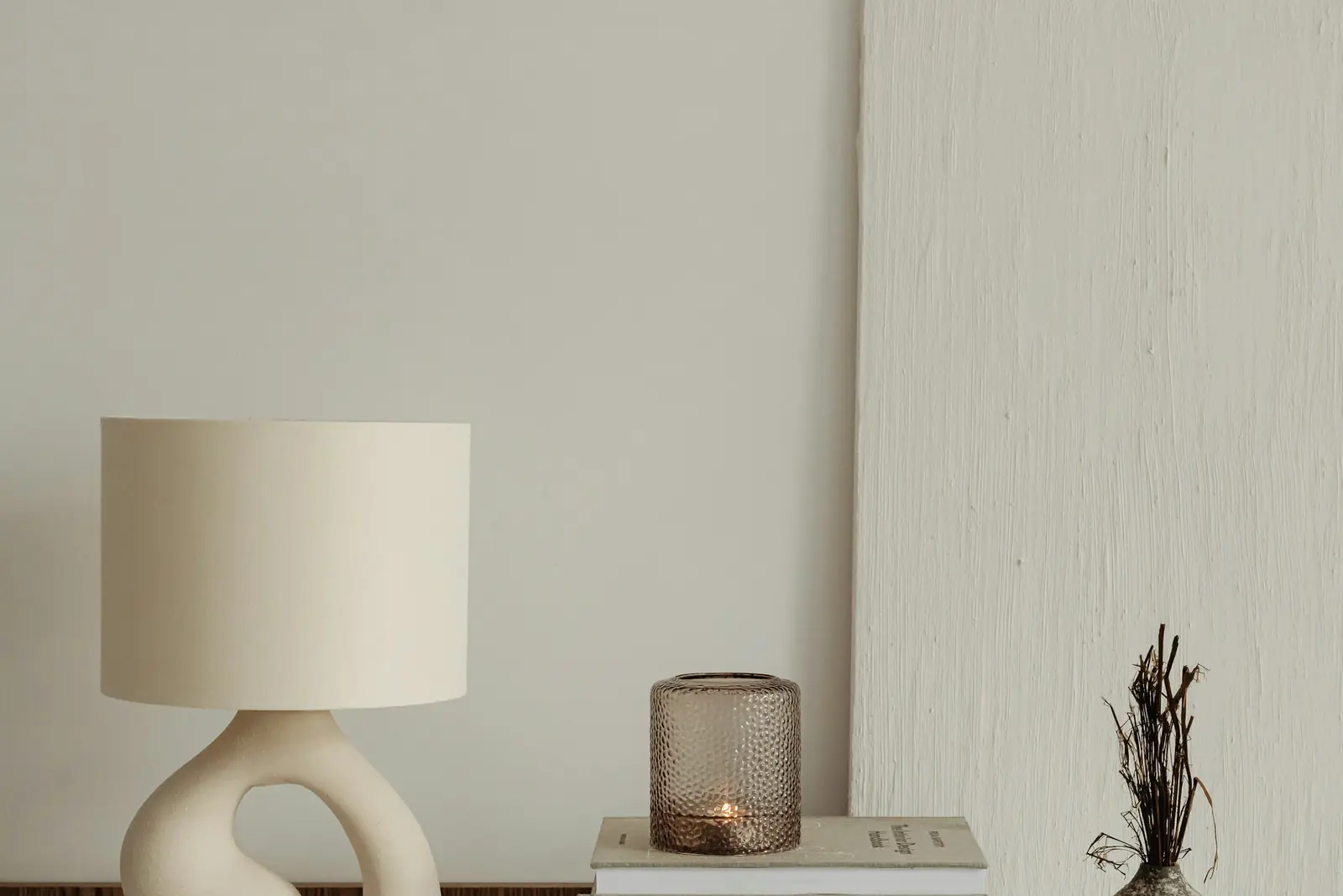 Sculptural ceramic table lamp, stacked books and a vase on a walnut sideboard