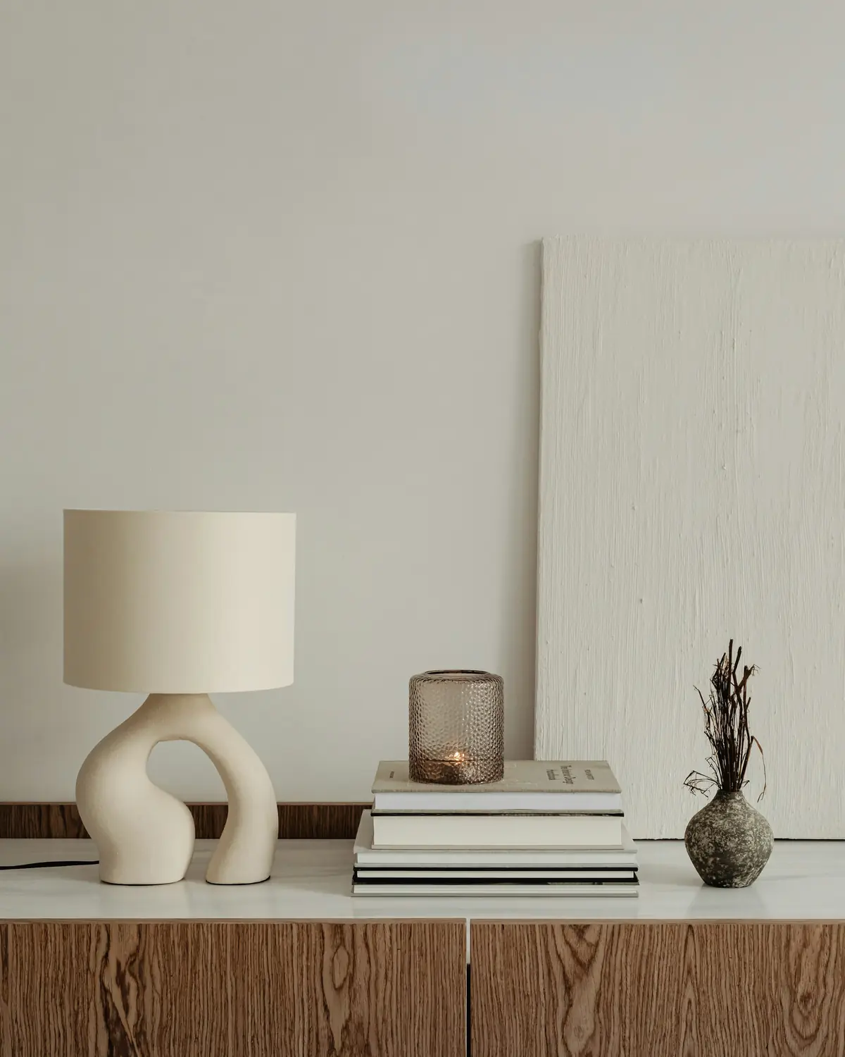 Sculptural ceramic table lamp, stacked books and a vase on a walnut sideboard