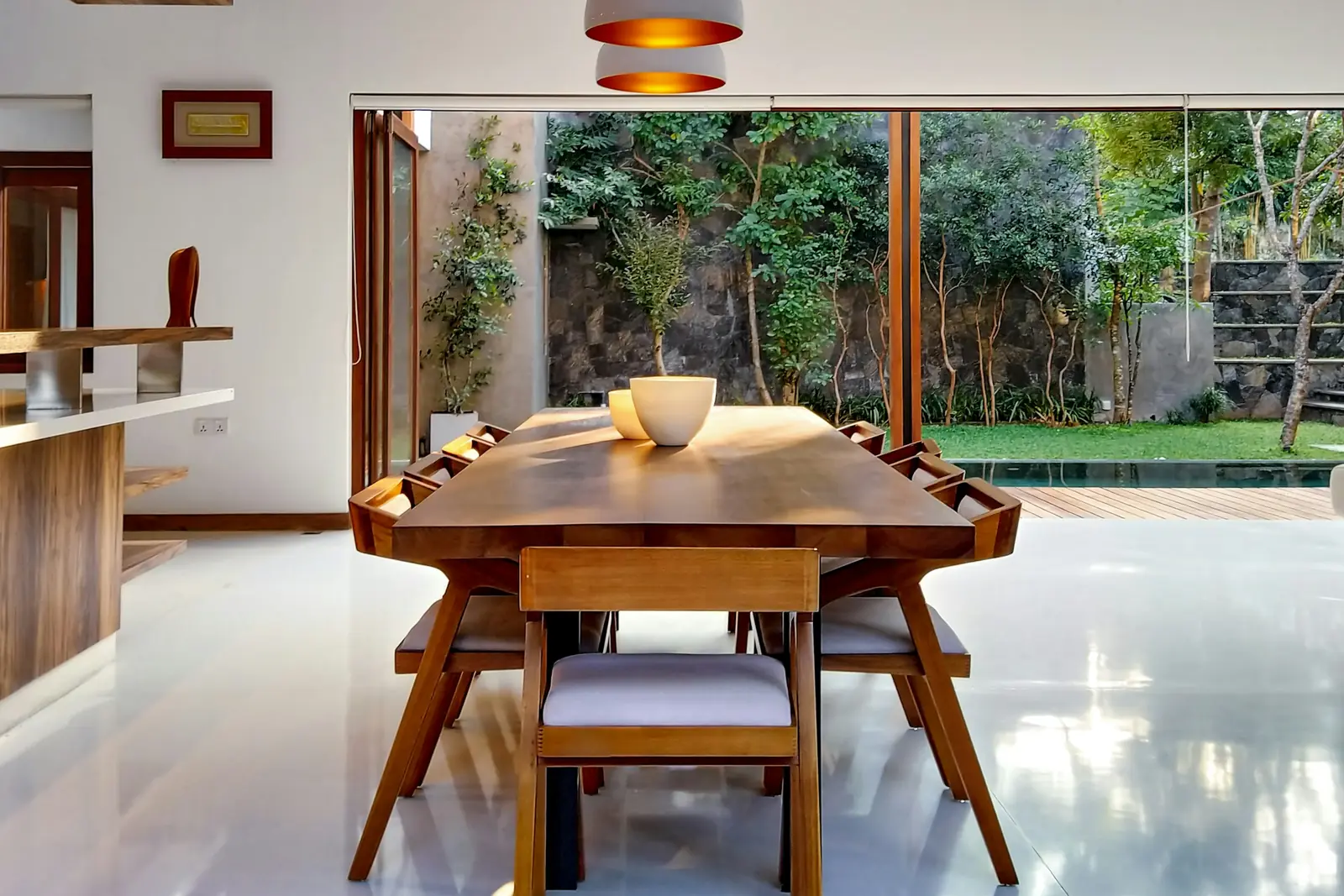 Mid-century wooden dining set beneath a layered pendant, opening onto a garden