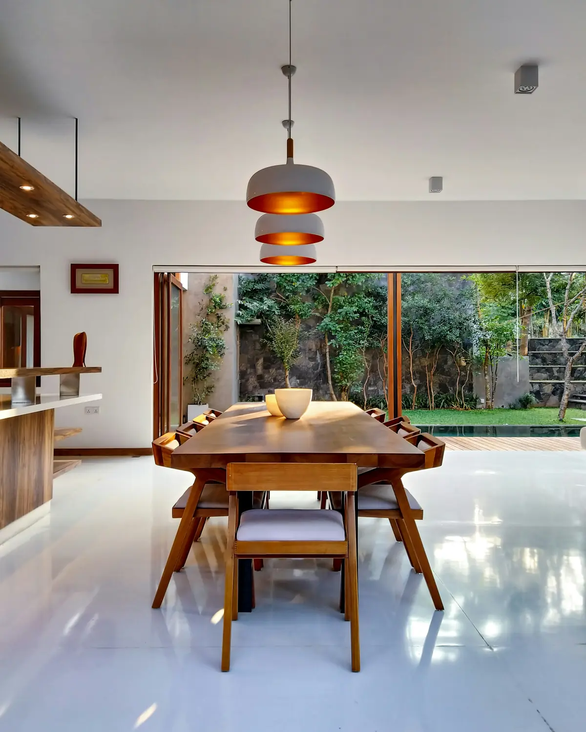 Mid-century wooden dining set beneath a layered pendant, opening onto a garden