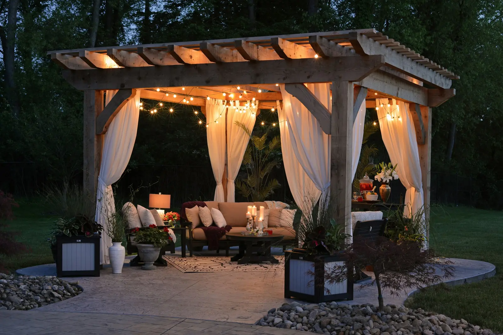 Timber pergola with draped curtains, string lights and outdoor seating at dusk