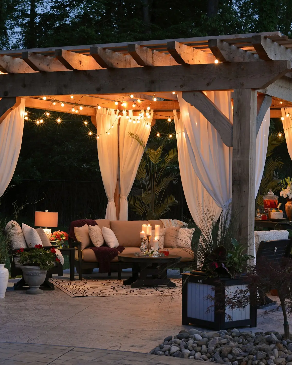 Timber pergola with draped curtains, string lights and outdoor seating at dusk
