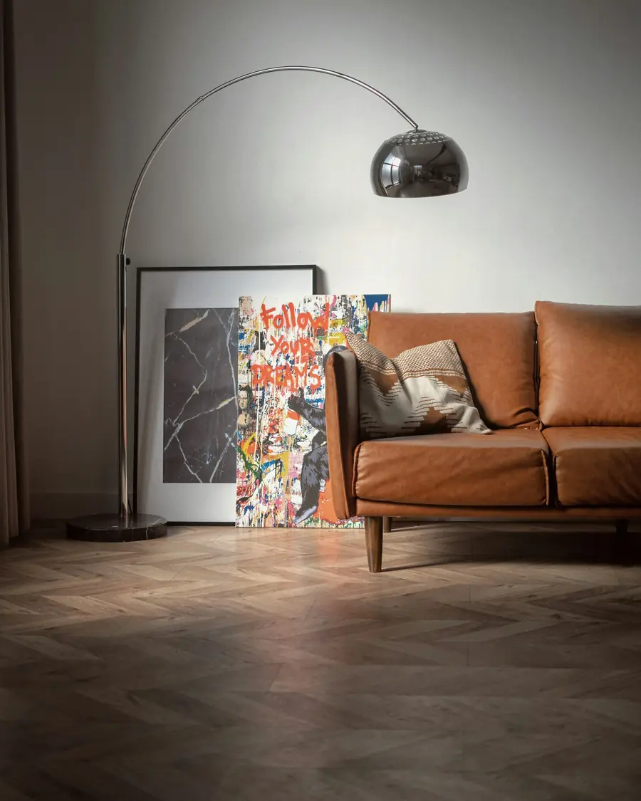 Brass arc floor lamp over a cognac leather sofa in a softly lit room