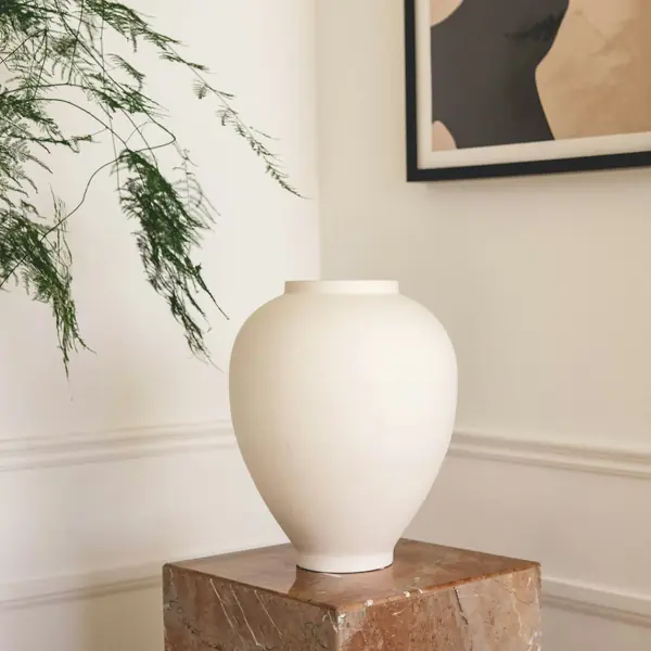 White ceramic vase on a marble plinth beside an abstract print