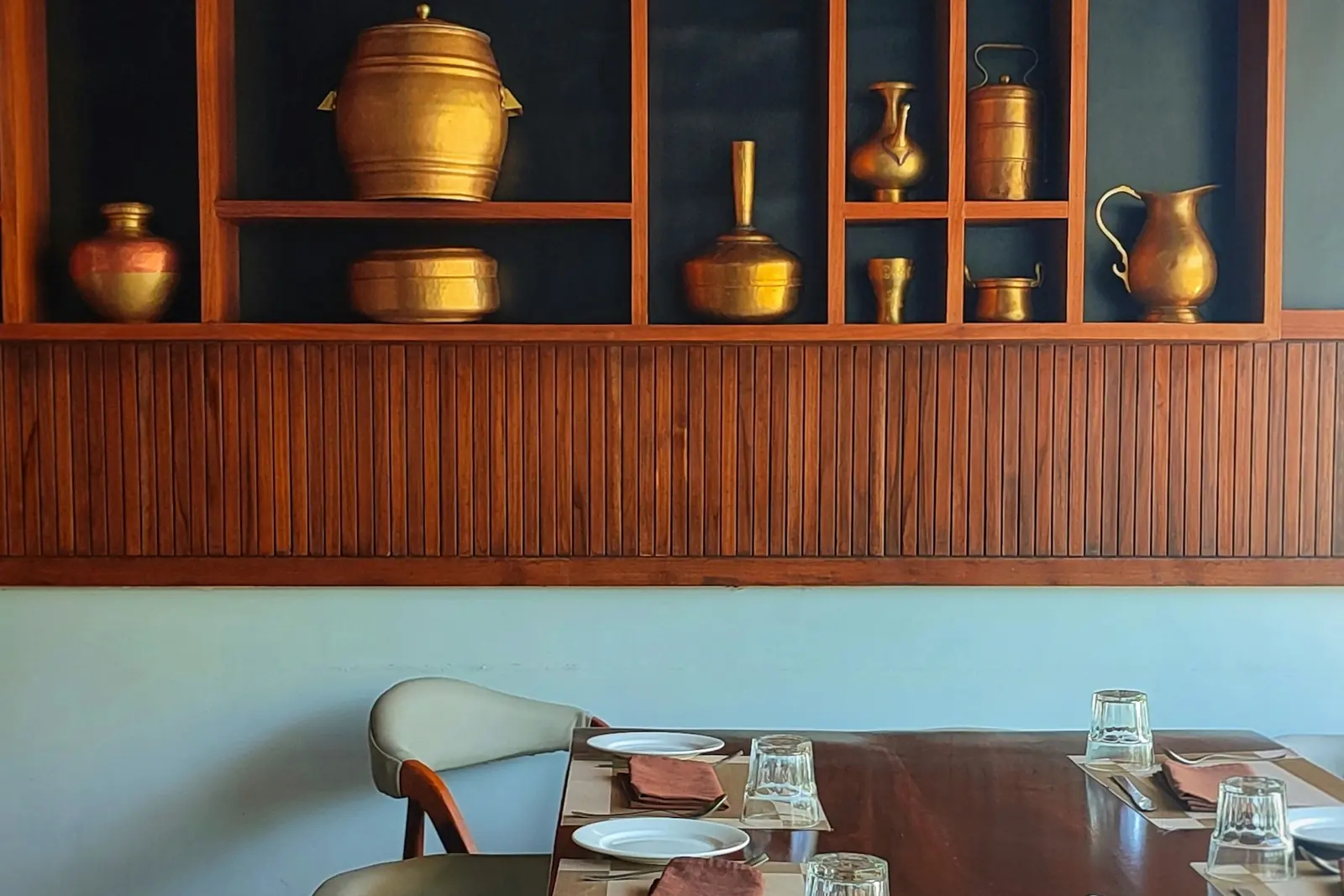 Solid wood display unit with brass vessels above a wooden dining table