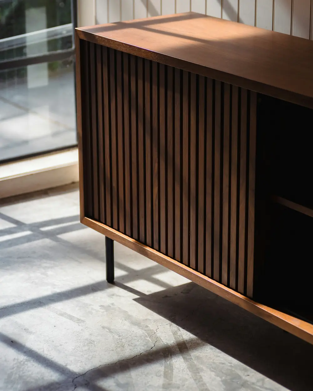Fluted solid-teak sideboard on slim black legs in a sunlit room