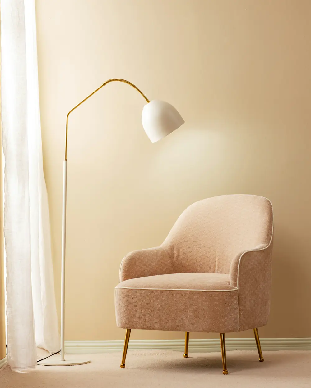 Arched brass floor lamp with a white dome shade beside a blush armchair