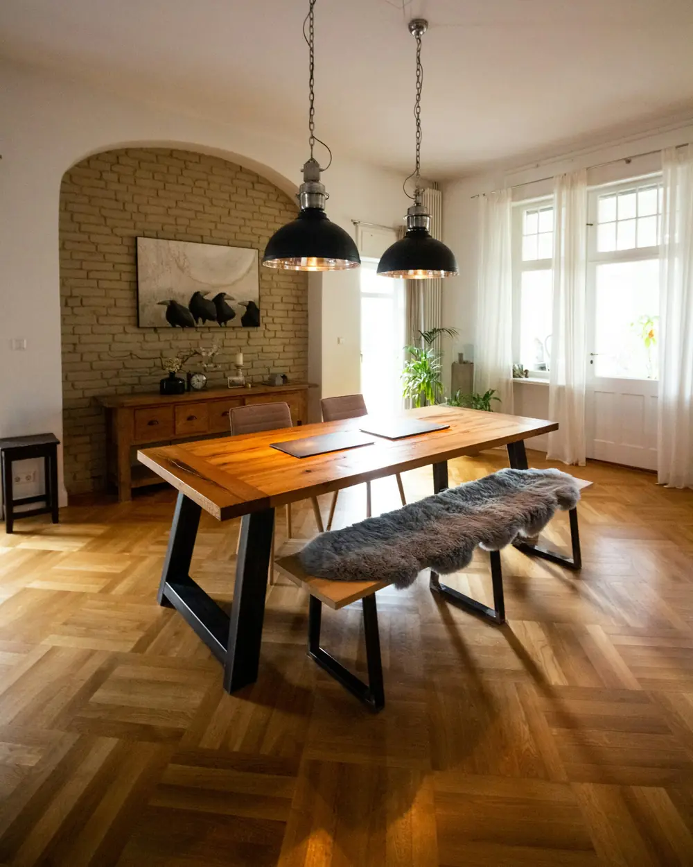 Live-edge wooden dining table on black steel legs with a bench, under twin pendant lights