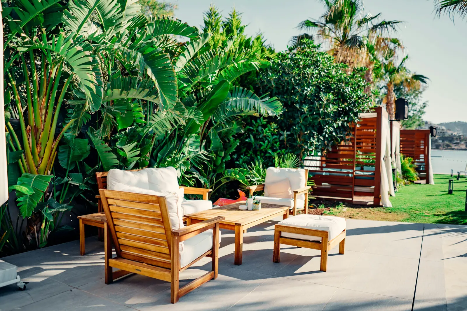 Teak outdoor lounge chairs with ivory cushions on a terrace framed by tropical plants