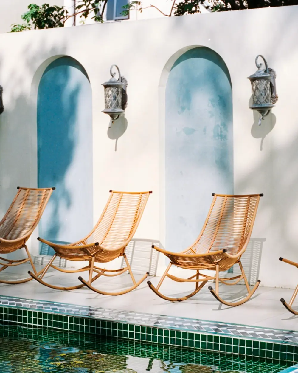Four cane rocking chairs beside a pool under arched white walls