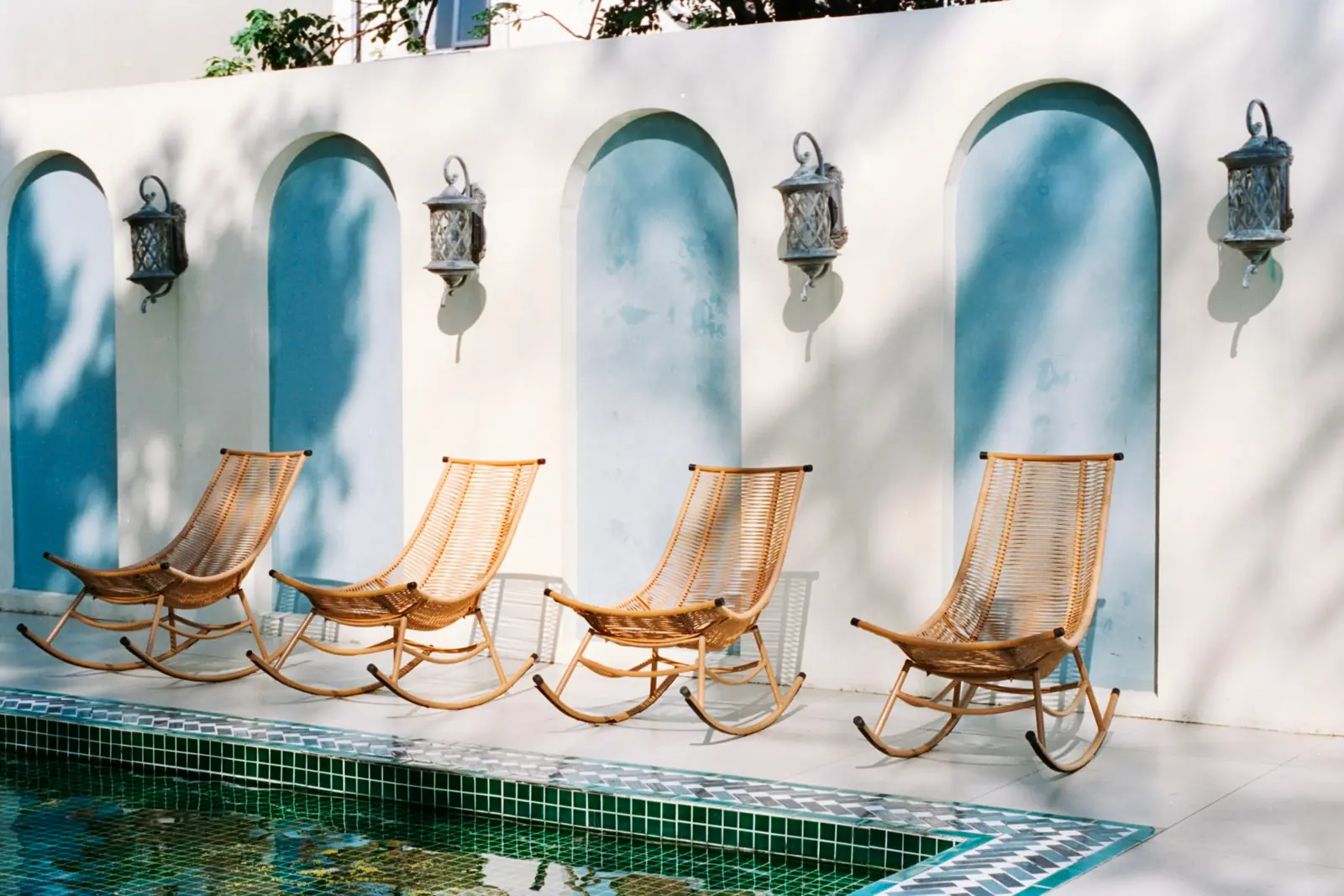 Four cane rocking chairs beside a pool under arched white walls