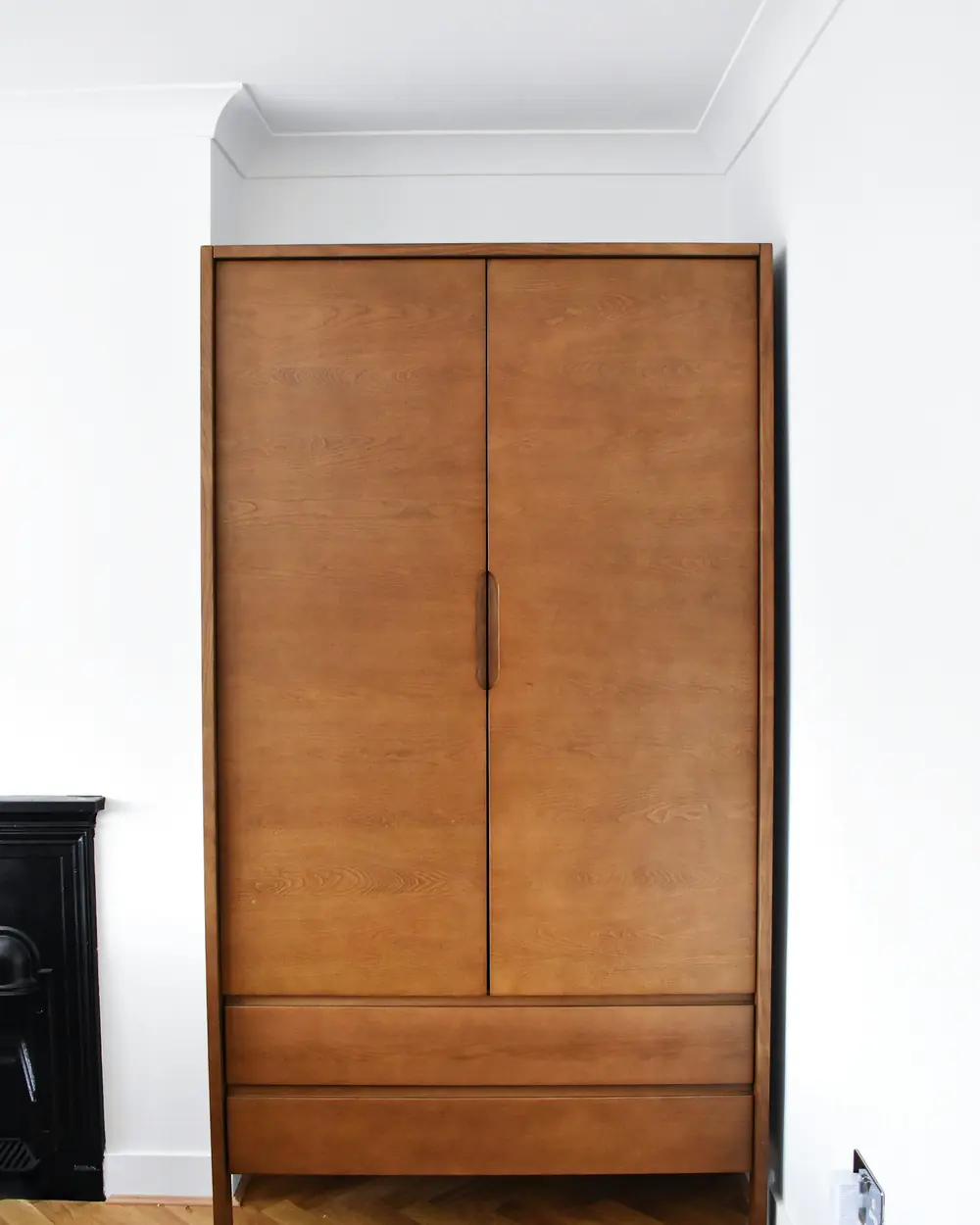 Two-door solid wood wardrobe with a plinth drawer on herringbone flooring