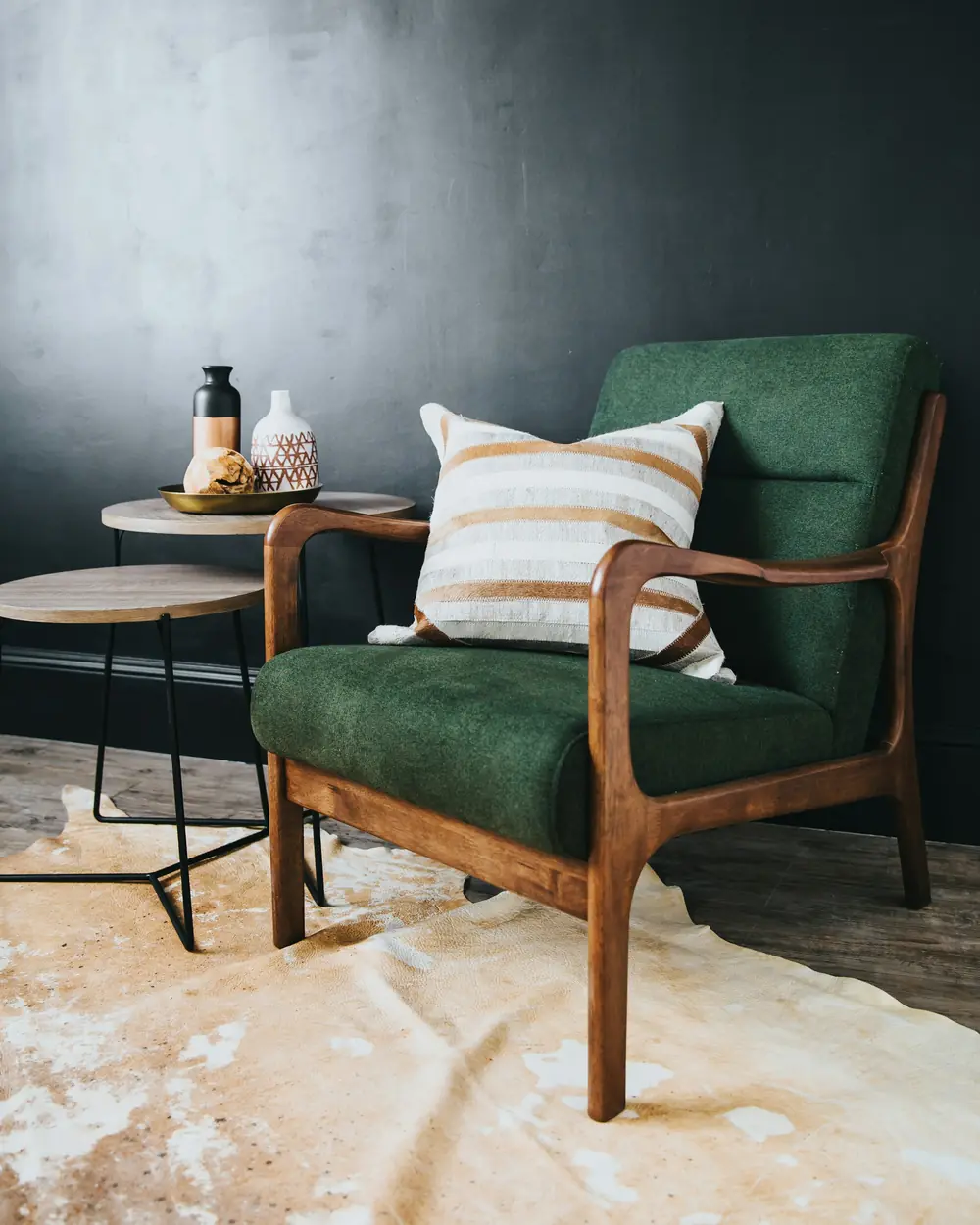 Bottle-green velvet lounge chair with a solid wood frame and striped cushion on a cowhide rug