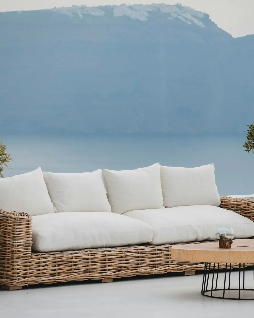 Hand-woven rattan outdoor sofa with white cushions on a terrace overlooking the sea
