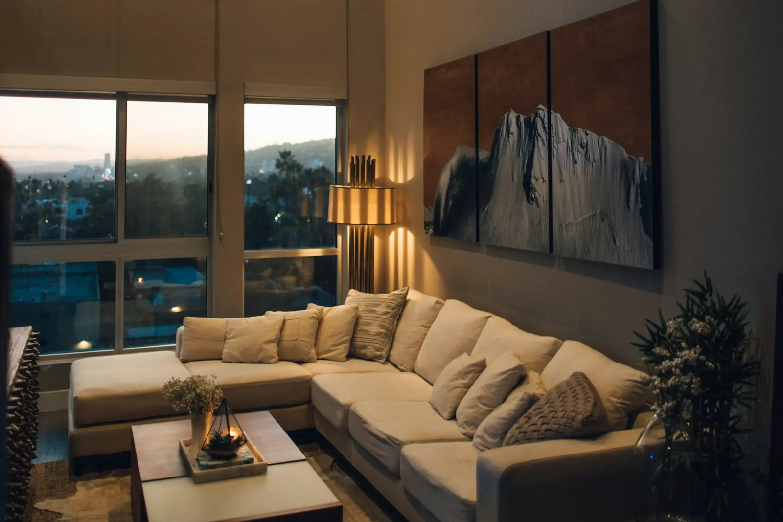 Double-height living room with a sectional sofa, large art and floor-to-ceiling windows at dusk