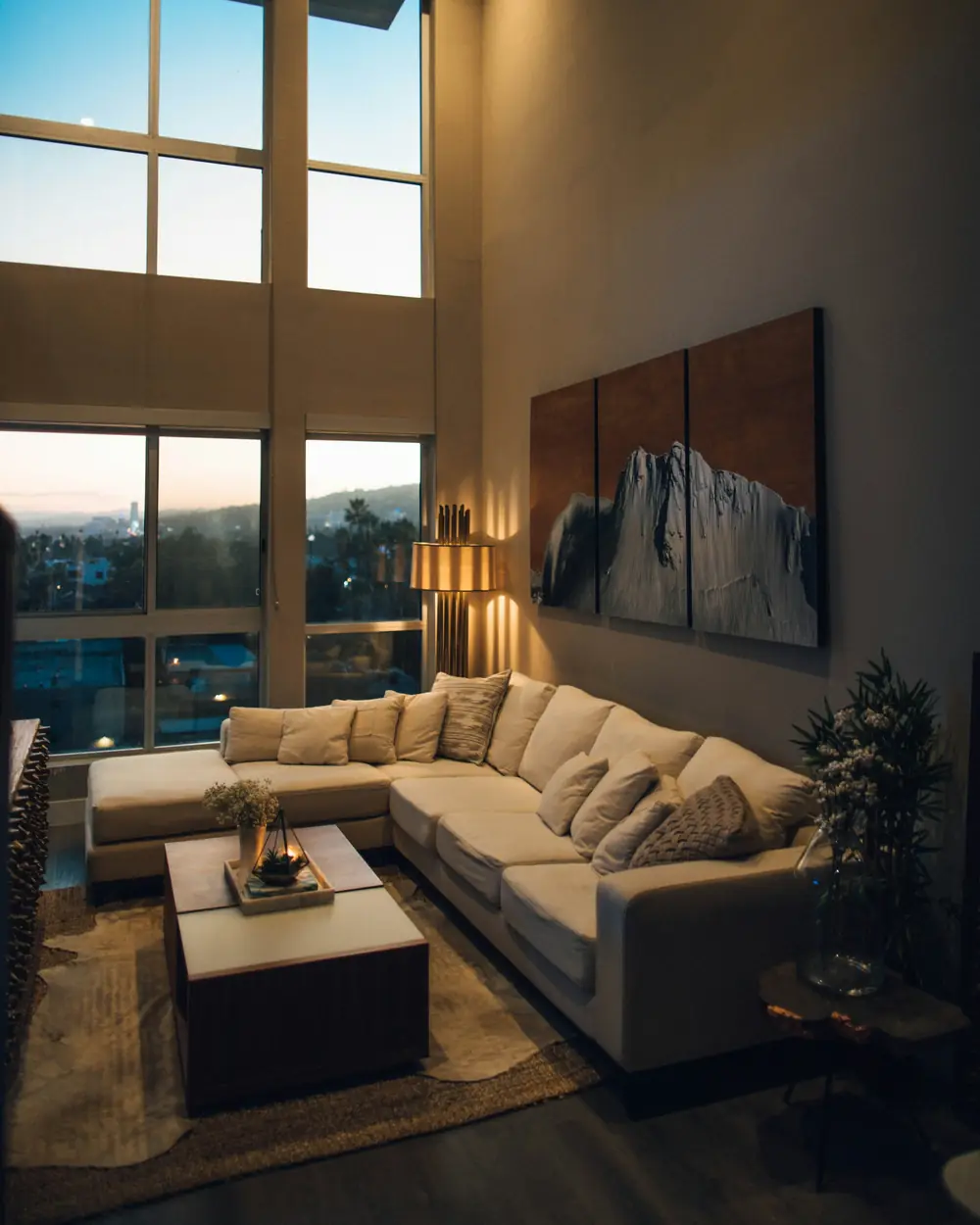Double-height living room with a sectional sofa, large art and floor-to-ceiling windows at dusk