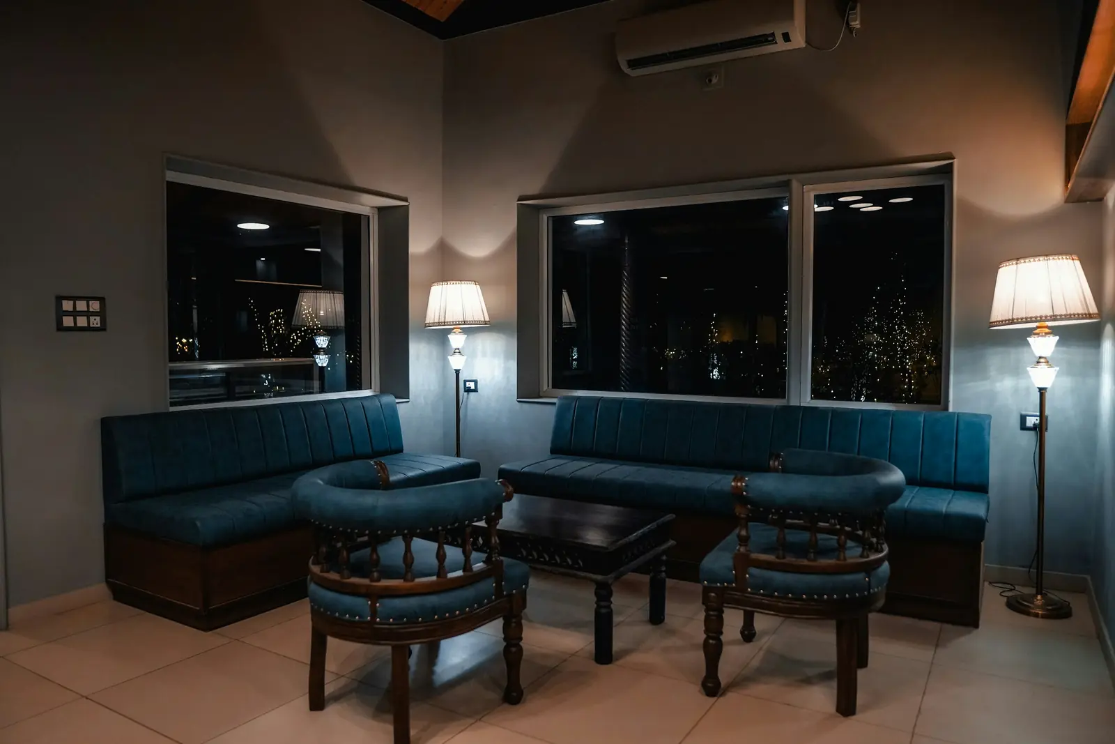 Studio lounge with navy upholstered seating, dark joinery and warm lamps at dusk