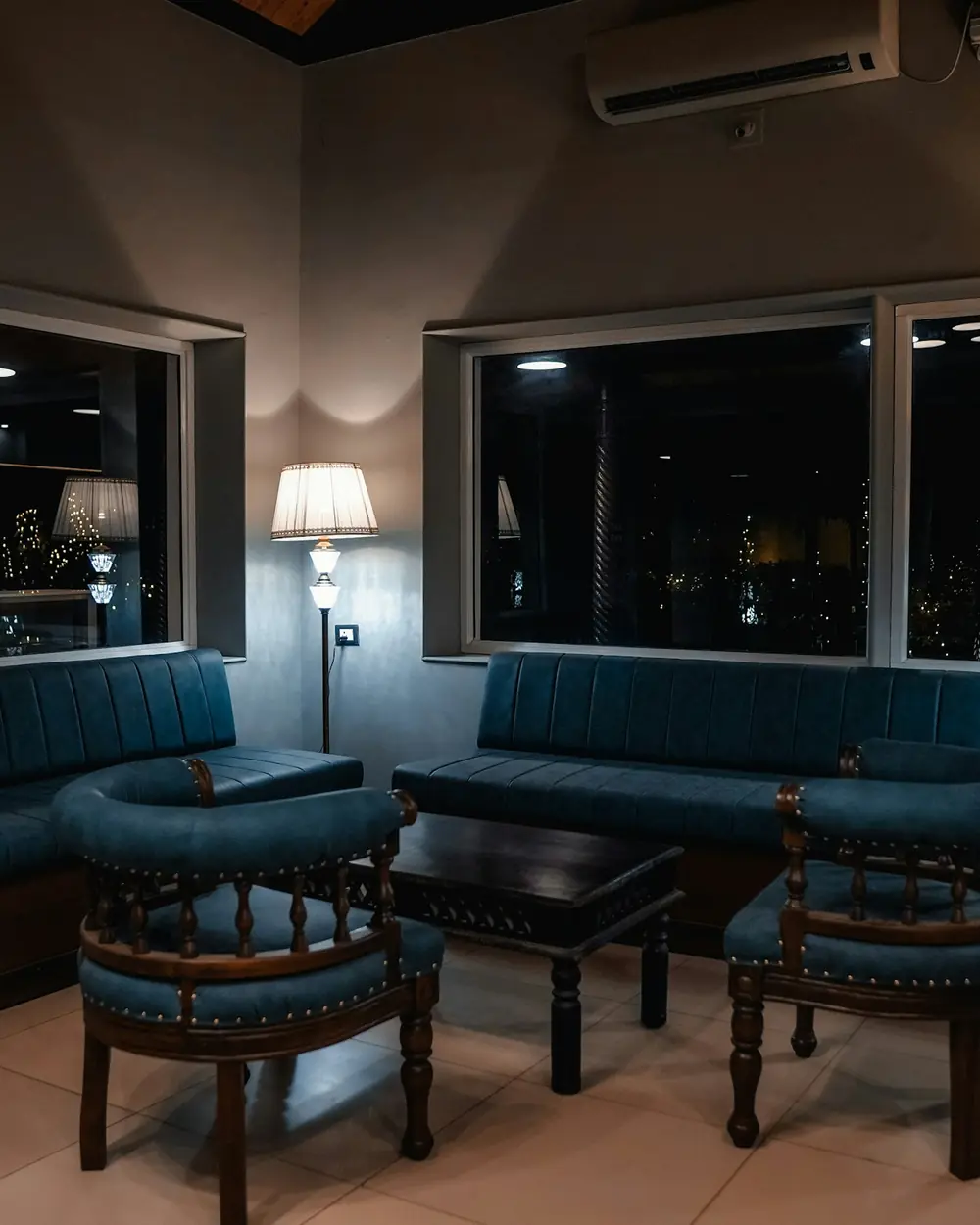 Studio lounge with navy upholstered seating, dark joinery and warm lamps at dusk